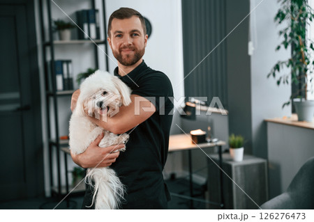 Modern office. Groomer is with Maltese dog indoors. Man is in the black uniform 126276473