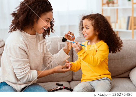 Cute Little Girl And Her Mother Having Fun Making Makeup Together Sitting On Couch At Home. Happy Family Moments Cute Little Girl And Her Mother Having Fun Making Makeup Together Sitting On Couch At Home. Happy Family Moments 126276486