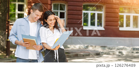 Portrait of cheerful couple of university friends laughing outdoors while checking classes schedule, reading information in notepad Portrait of cheerful couple of university friends laughing outdoors while checking classes schedule, reading information in notepad 126276489