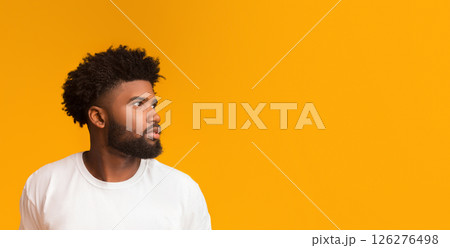 Skeptical young african american man looking aside at free space on orange background Skeptical young african american man looking aside at free space on orange background 126276498