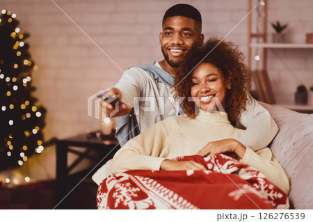 Afro couple in love at Christmas eve enjoy watching tv, lying under plaid on sofa 126276539