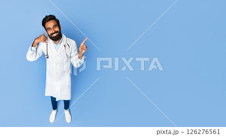 A smiling Indian doctor with a beard is wearing a white coat and stethoscope. He is gesturing with his hands, making a call gesture with his left hand and pointing at copy space A smiling Indian doctor with a beard is wearing a white coat and stethoscope. He is gesturing with his hands, making a call gesture with his left hand and pointing at copy space 126276561