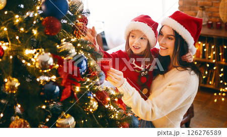 Mother and daughter in Santa hats decorating beautiful xmas tree at home Mother and daughter in Santa hats decorating beautiful xmas tree at home 126276589