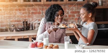 Happy girl holding tray and smelling freshly baked croissants, cooking with mom, kitchen interior, copy space 126276592