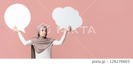 Difficult choice. Muslim girl in hijab holding two empty speech bubbles over pink background, free space Difficult choice. Muslim girl in hijab holding two empty speech bubbles over pink background, free space 126276603