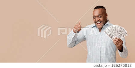 Excited middle aged afro man enjoying big jackpot, showing thumb up with lots of money, orange studio background Excited middle aged afro man enjoying big jackpot, showing thumb up with lots of money, orange studio background 126276812