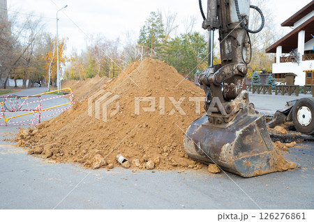 Construction equipment digs earthen trench. excavator with bucket near a mound of dirt. excavation work on a construction site on a road 126276861