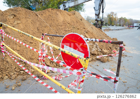 A construction barrier made of yellow metal with a red stop sign is surrounded by caution tape, roadwork taking place 126276862