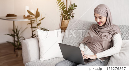 Young muslim woman in hijab using laptop computer at home, typing on keyboard, answering emails, chatting with friends online. Young muslim woman in hijab using laptop computer at home, typing on keyboard, answering emails, chatting with friends online. 126276867