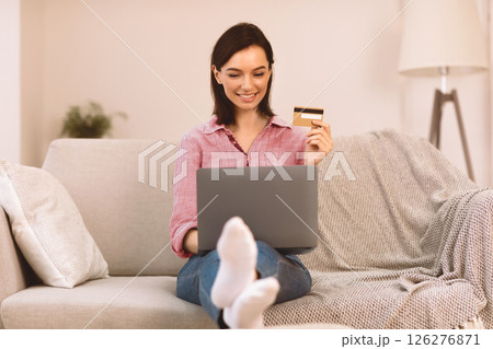 Online Banking. Satisfied girl making purchases on internet using laptop and credit card to pay, sitting on sofa Online Banking. Satisfied girl making purchases on internet using laptop and credit card to pay, sitting on sofa 126276871
