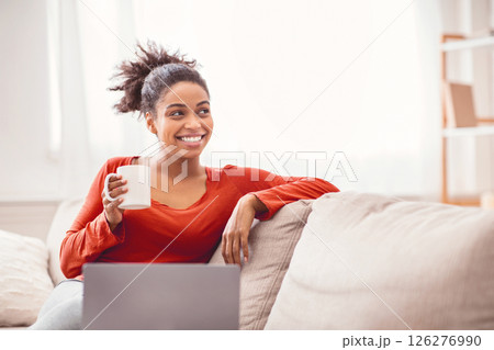 Smiling African American Lady With Laptop Having Coffee Sitting On Sofa At Home. Enjoying Weekend Morning. Empty Space 126276990