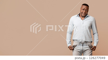 Coronacrisis concept. Sad mature african american man showing empty pockets, orange studio background Coronacrisis concept. Sad mature african american man showing empty pockets, orange studio background 126277049