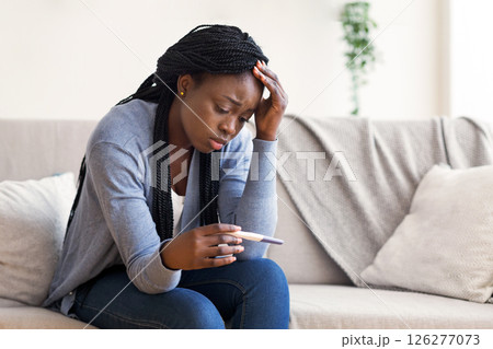 Unintended pregnancy. Depressed african american woman upset with positive test results, sitting on couch at home with sad face expression 126277073