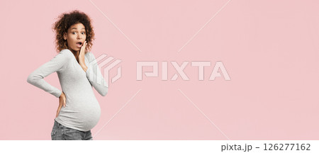 Surprised black pregnant woman closing mouth and looking at camera over pink background 126277162