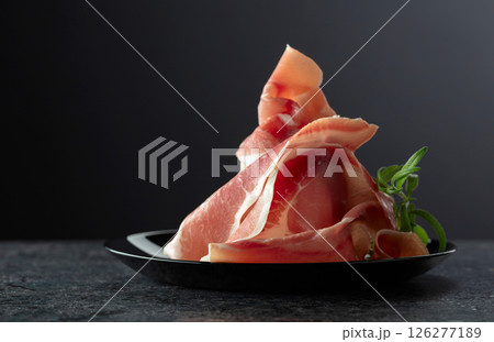 Italian prosciutto crudo with rosemary on a black plate. 126277189