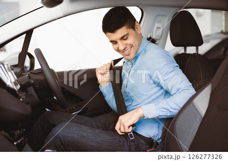 Driving Regulations. Guy Putting On Seat Belt Sitting In New Car In Dealership Center. Selective Focus Driving Regulations. Guy Putting On Seat Belt Sitting In New Car In Dealership Center. Selective Focus 126277326