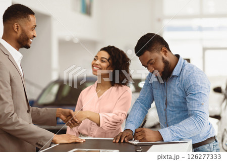 Buying New Car. African American Spouses Shaking Hands With Auto Seller Signing Papers In Dealership Office. Selective Focus 126277333