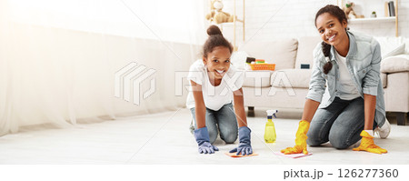 Two adorable african girls cleaning carpet at home, helping parents to keep house tidy, copy space 126277360