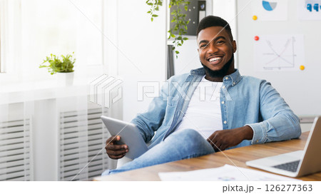 Ready for presentation. Portrait of black millennial employee holding digital tablet, sitting at workplace and looking at camera Ready for presentation. Portrait of black millennial employee holding digital tablet, sitting at workplace and looking at camera 126277363