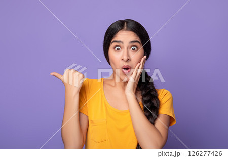 Wow, Look Here. Amazed young indian woman pointing at copy space over purple studio background. Excited surprised lady indicating free space, showing place for advert or promotional text 126277426