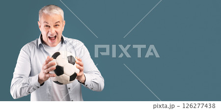 Mature Football Player. Excited cheering middle aged man posing with soccer ball on blue studio wall, panorama with copyspace Mature Football Player. Excited cheering middle aged man posing with soccer ball on blue studio wall, panorama with copyspace 126277438