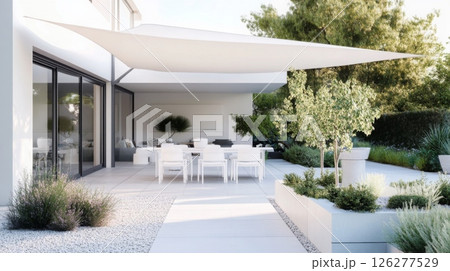 A modern outdoor dining area boasts white furniture beneath a sleek shade sail, surrounded by greenery and decorative plants, creating a serene space for gatherings. 126277529