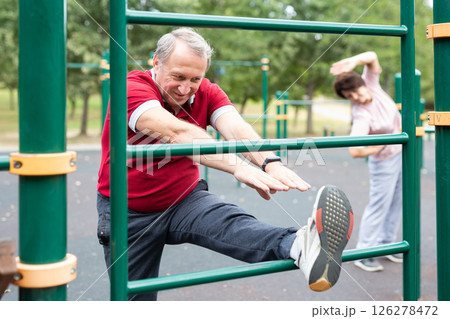 Elderly man doing stretching exercises on a sports bar at an outdoor sports ground Elderly man doing stretching exercises on a sports bar at an outdoor sports ground 126278472