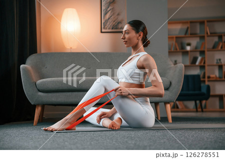 Young woman with slim body type in white sportswear is indoors doing yoga 126278551
