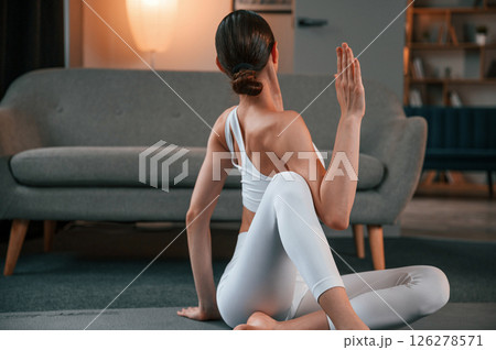 Young woman with slim body type in white sportswear is indoors doing yoga 126278571