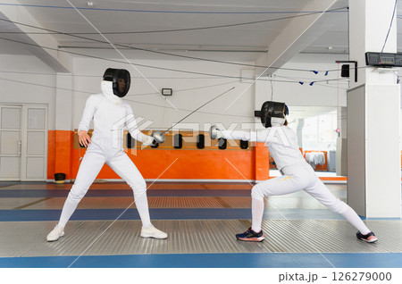 Female fencer lunging with extended sword in indoor match. Female fencer lunging with extended sword in indoor match. 126279000