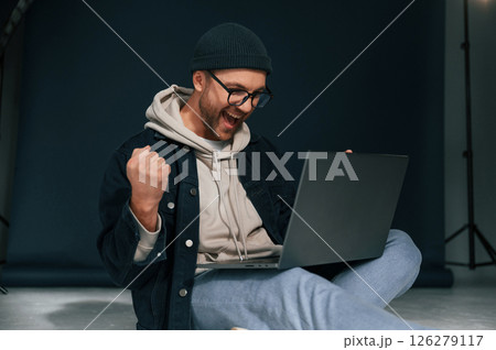 Celebrating success. Feeling uplifting. Using laptop. Handsome man is in the studio against background Celebrating success. Feeling uplifting. Using laptop. Handsome man is in the studio against background 126279117