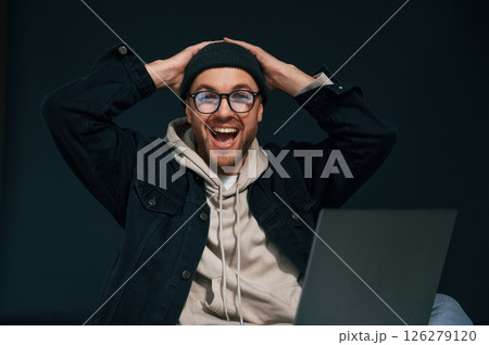 Celebrating success. Feeling uplifting. Using laptop. Handsome man is in the studio against background Celebrating success. Feeling uplifting. Using laptop. Handsome man is in the studio against background 126279120
