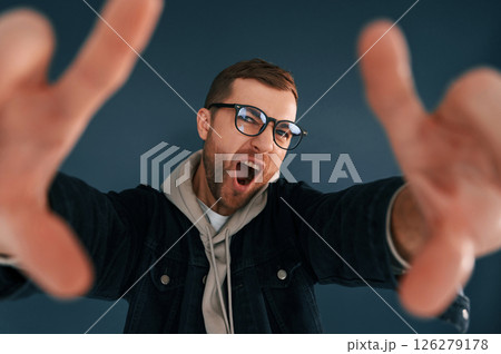 Guy is pretending that he's doing photoshoot by using hands gestures. Handsome man is in the studio against blue background 126279178