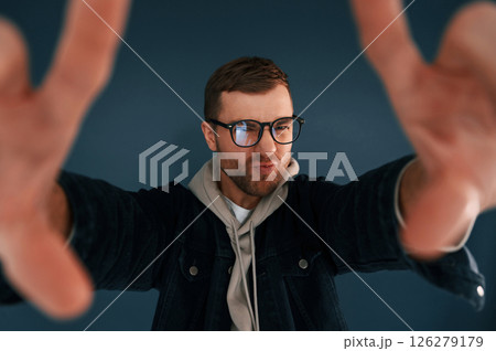 Guy is pretending that he's doing photoshoot by using hands gestures. Handsome man is in the studio against blue background Guy is pretending that he's doing photoshoot by using hands gestures. Handsome man is in the studio against blue background 126279179