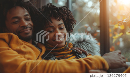 A couple sits on a couch by a window, smiling and enjoying each other's company. A couple sits on a couch by a window, smiling and enjoying each other's company. 126279405
