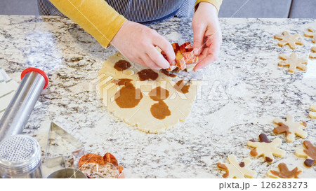 Using various festive cookie cutters, we're cutting out charming gingerbread cookies from the rolled dough on the sleek marble counter, bringing holiday cheer to the modern kitchen. 126283273