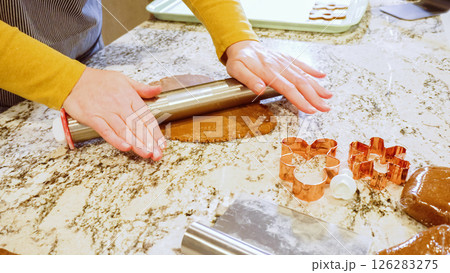 Using an adjustable rolling pin to roll out gingerbread cookie dough on the elegant marble counter in a modern kitchen, getting ready for festive holiday baking. Using an adjustable rolling pin to roll out gingerbread cookie dough on the elegant marble counter in a modern kitchen, getting ready for festive holiday baking. 126283275