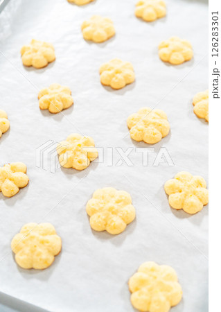 Golden lemon spritz cookies rest on a sheet of parchment paper, showcasing their delicate floral shape and light, crisp texture. These buttery cookies are infused with bright citrus flavor, making Golden lemon spritz cookies rest on a sheet of parchment paper, showcasing their delicate floral shape and light, crisp texture. These buttery cookies are infused with bright citrus flavor, making 126283301