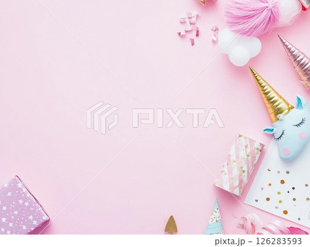 A whimsical arrangement of pastel-colored unicorn-themed party decorations and candy, set against a pink background. The setup includes a unicorn figure, lollipops, and sweets, creating a fun and 126283593