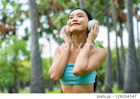 Asian sports woman listening to music on headphones outdoors 126284347