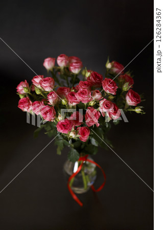 Beautiful bouquet of pink (red) roses bushes with water drops on a black background. Selective focus, close-up. 126284367