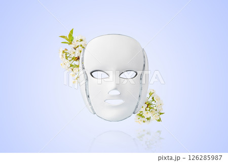 Cosmetic LED facial mask regenerative treatment with cherry blossom twigs on a gradient blue background. Health and beauty of the face. Taking care of yourself and your face, anti-aging, prolonging 126285987