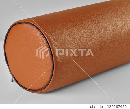 Close-up of a bolster cushion with orange eco-leather upholstery resting on a light gray surface Close-up of a bolster cushion with orange eco-leather upholstery resting on a light gray surface 126287423
