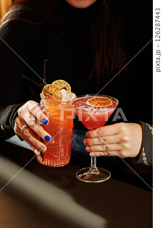 Woman holding two fancy cocktails with orange garnish in a tiki mug and martini glass Woman holding two fancy cocktails with orange garnish in a tiki mug and martini glass 126287443