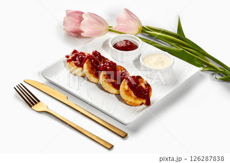 Syrniki with jam, sour cream and pink tulips on white background 126287838