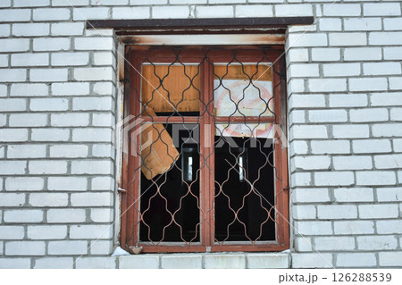 Broken window with an old wooden frame on a white brick wall of a closed house. Broken window with an old wooden frame on a white brick wall of a closed house. 126288539