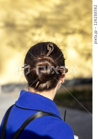 Woman with styled bun and hairpin outdoors in sunlight wearing a blue coat Woman with styled bun and hairpin outdoors in sunlight wearing a blue coat 126288562