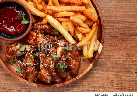barbecue chicken wings, sprinkled with sesame seeds, with French fries, and sauce, on a wooden plate, rustic style, barbecue chicken wings, sprinkled with sesame seeds, with French fries, and sauce, on a wooden plate, rustic style, 126289213