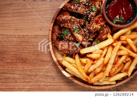 barbecue chicken wings, sprinkled with sesame seeds, with French fries, and sauce, on a wooden plate, rustic style, barbecue chicken wings, sprinkled with sesame seeds, with French fries, and sauce, on a wooden plate, rustic style, 126289214