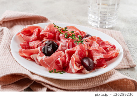 Freshly cut dried meat, served with olives and herbs, on a white plate, light background, no people, 126289230